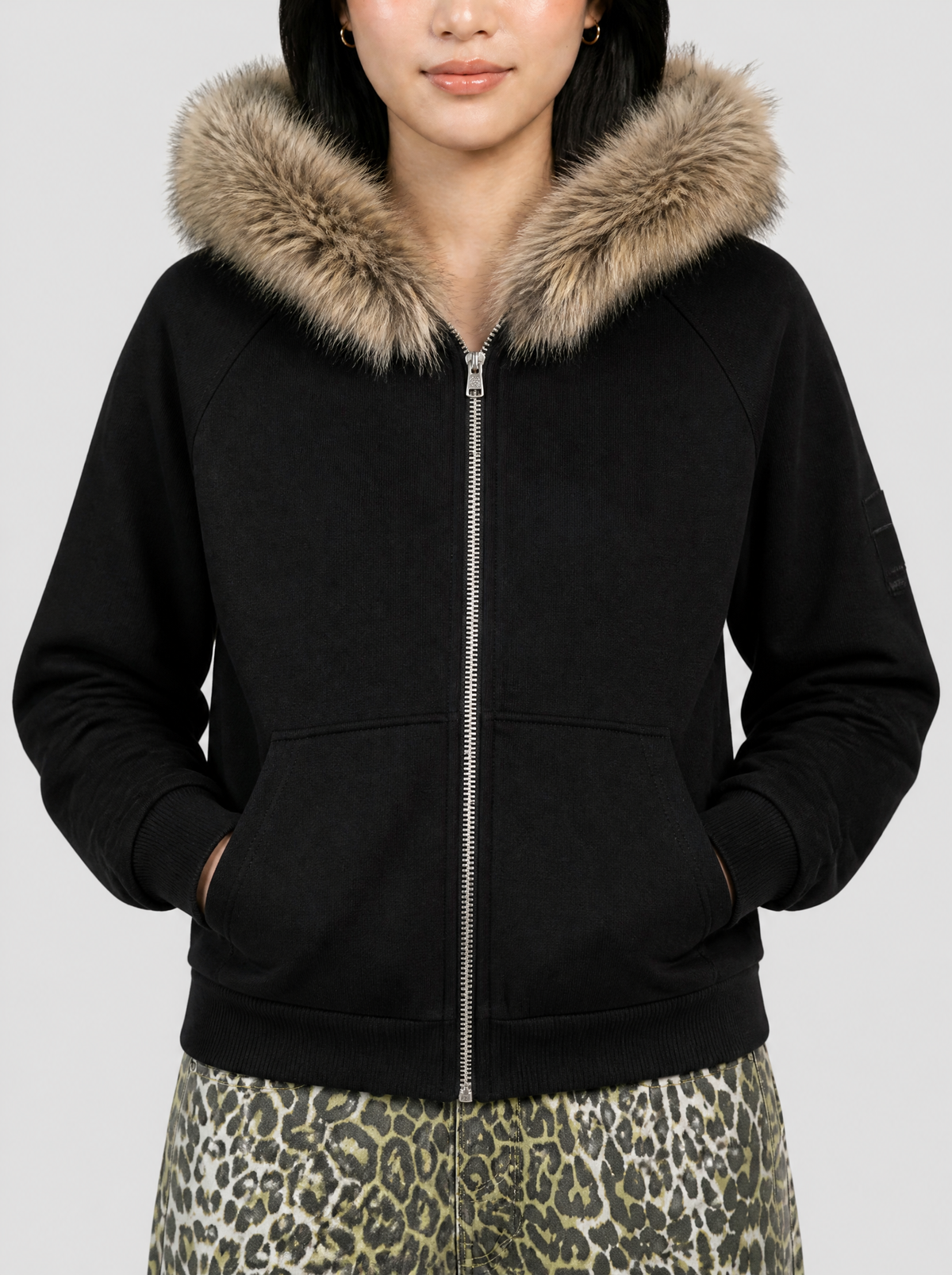 Photo détail | Gros plan sur la capuche en fausse fourrure beige du sweat zippé noir et sur son zip argenté, porté par une femme | Variante : Noir