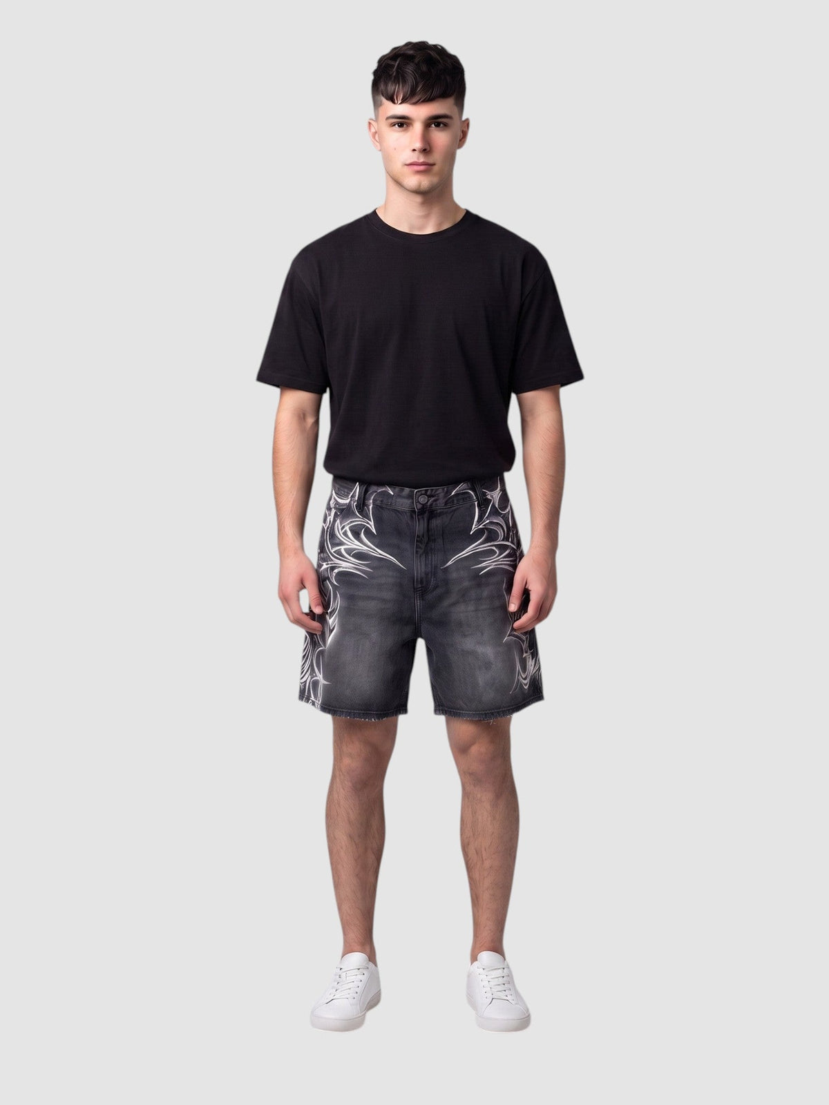 Short en denim noir avec motifs tribaux blancs aérographiés, ourlet brut et coupe ample, sur un modèle homme.