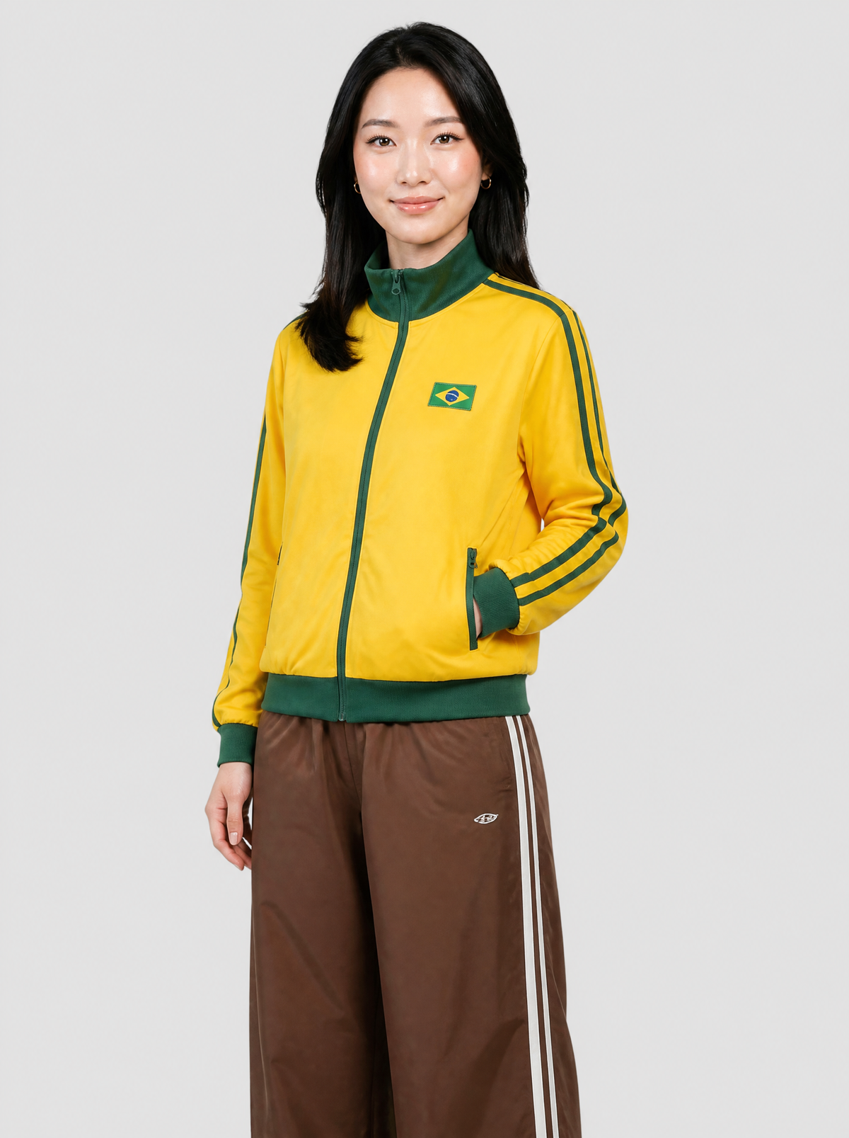 Autre vue | Femme de trois quarts en veste de survêtement jaune à bandes vertes et écusson drapeau du Brésil, avec un jogging marron