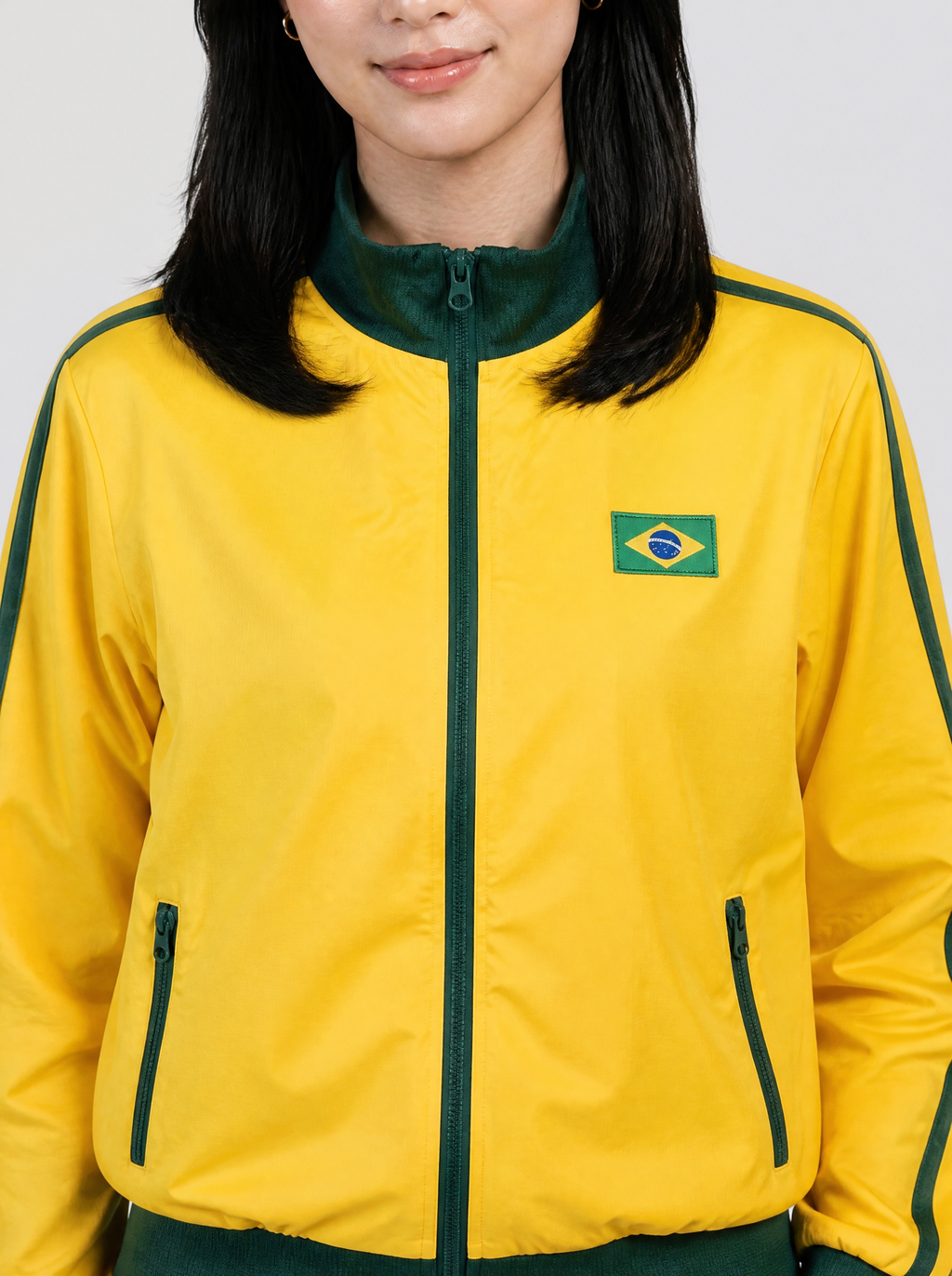 Photo détail | Gros plan sur la veste jaune : col montant vert, zip vert, double bande verte à l'épaule et petit drapeau brésilien