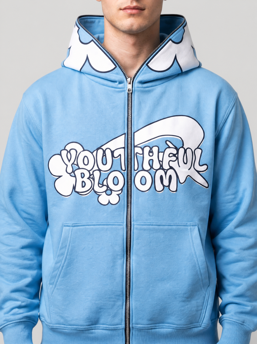 Photo détail | Gros plan sur le sweat bleu ciel : lettres bulles blanches Youthful Bloom coupées par le zip et pétales blancs de la capuche