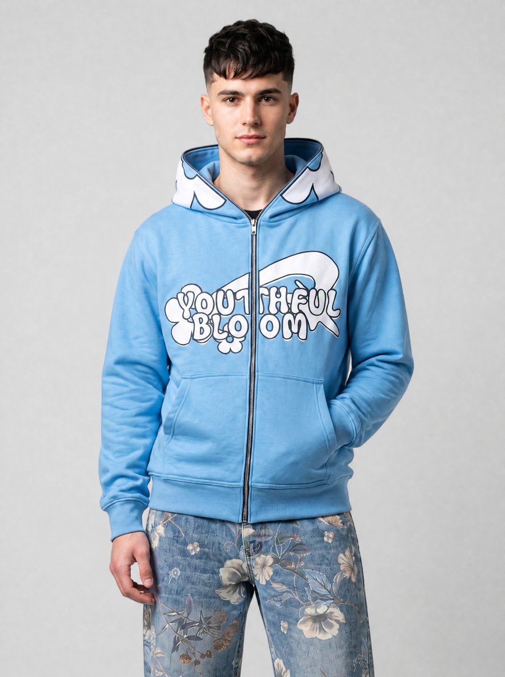 Autre vue | Homme de face en veste zippée bleu clair à inscription bulle Youthful Bloom et capuche à pétales, avec un jean fleuri