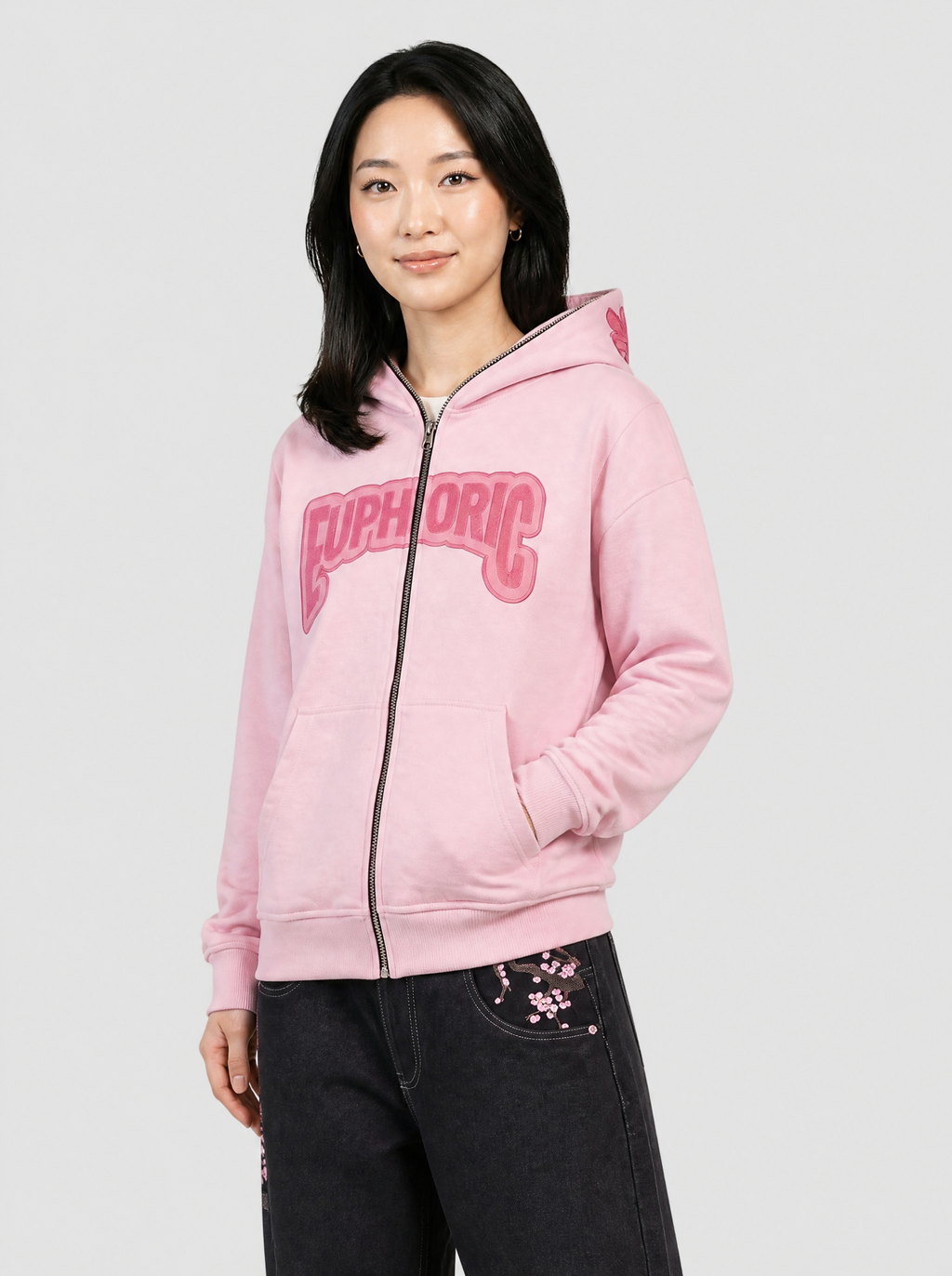 Autre vue | Femme de trois quarts en sweat zippé rose pastel capuche relevée, lettrage Euphoric framboise, avec un jean noir