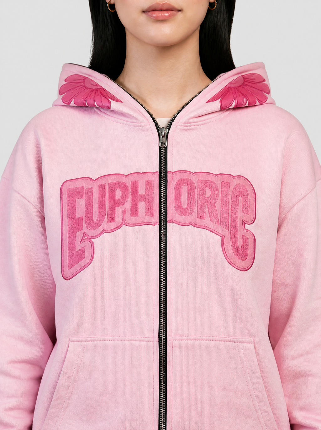 Photo détail | Gros plan sur le sweat rose pastel : lettres Euphoric framboise en arc coupées par le zip et pétales roses de la capuche