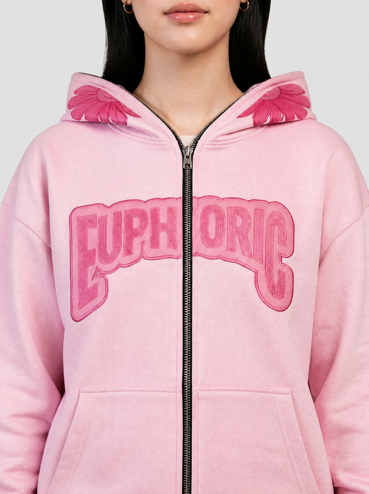 Photo détail | Gros plan sur le sweat rose pastel : lettres Euphoric framboise en arc coupées par le zip et pétales roses de la capuche