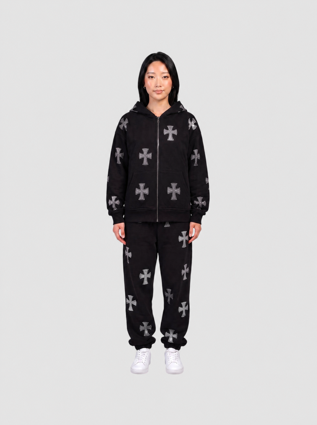 Ensemble hoodie zippé noir longueur hanches et jogging noir à motifs croix gothiques gris, porté de face par une femme.