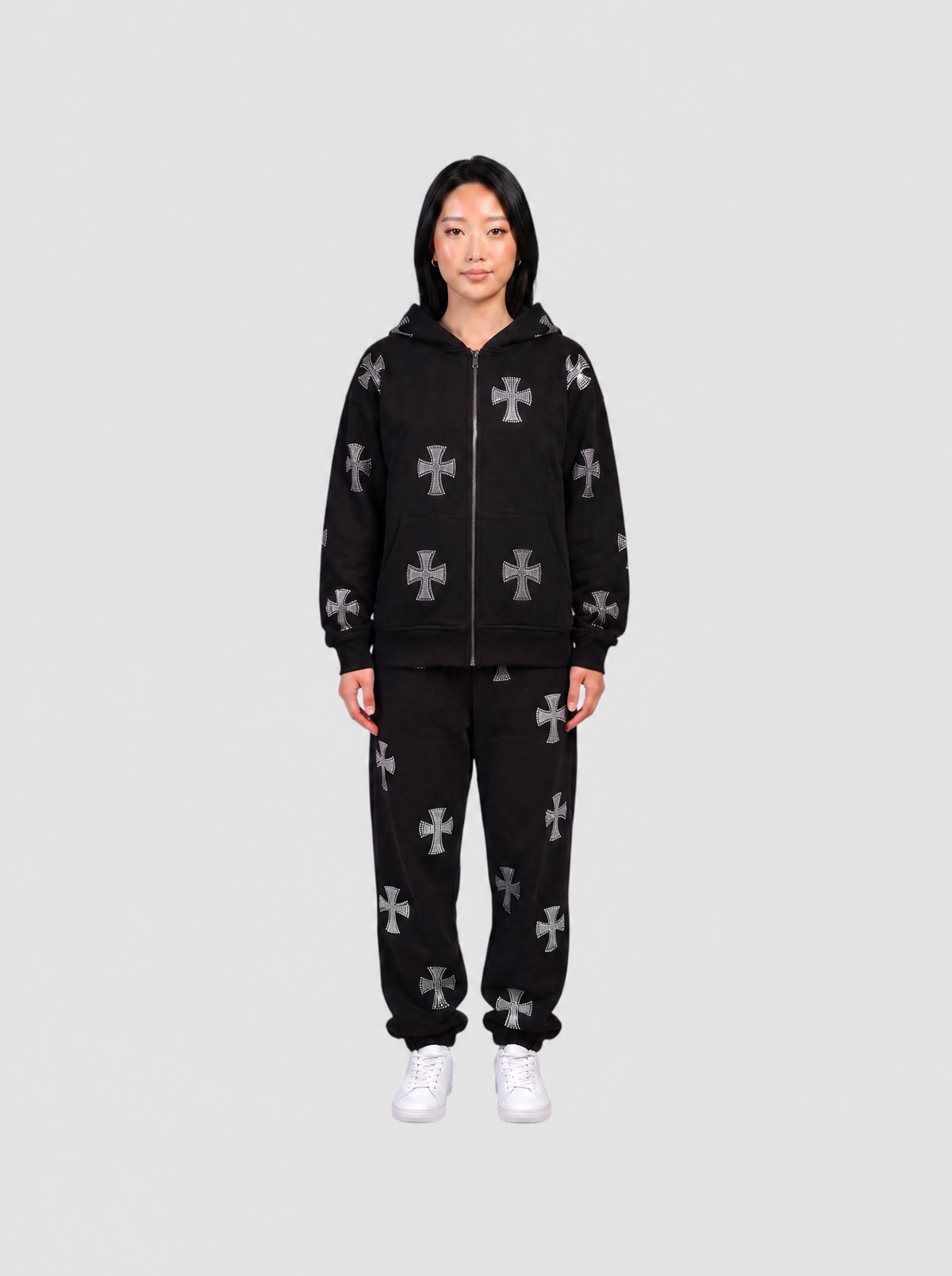 Ensemble hoodie zippé noir longueur hanches et jogging noir à motifs croix gothiques gris, porté de face par une femme.