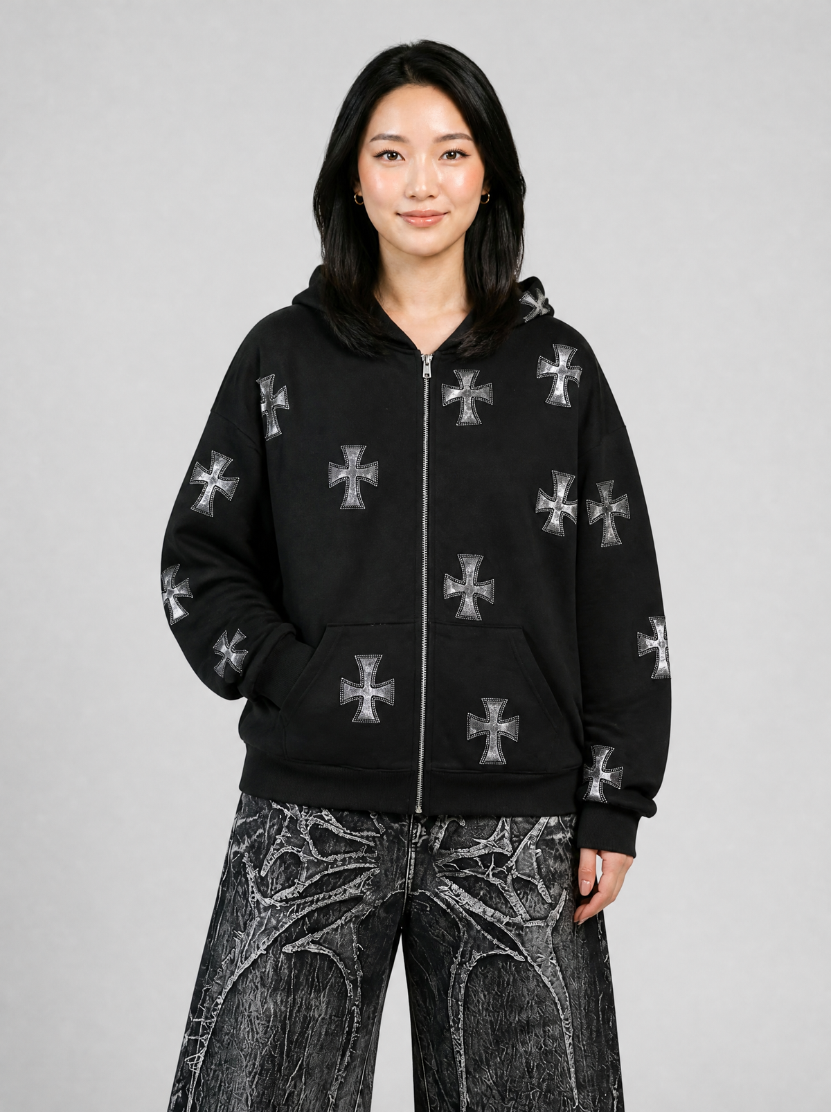 Autre vue | Femme de face en veste zippée noire à capuche, longueur hanches, croix gothiques scintillantes et poches kangourou, avec un jean large noir | Variante : Noir