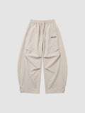 Y2K Avenue beige oversized nylon joggers with elastic waist, side pockets, and white embroidered script logo on thigh.