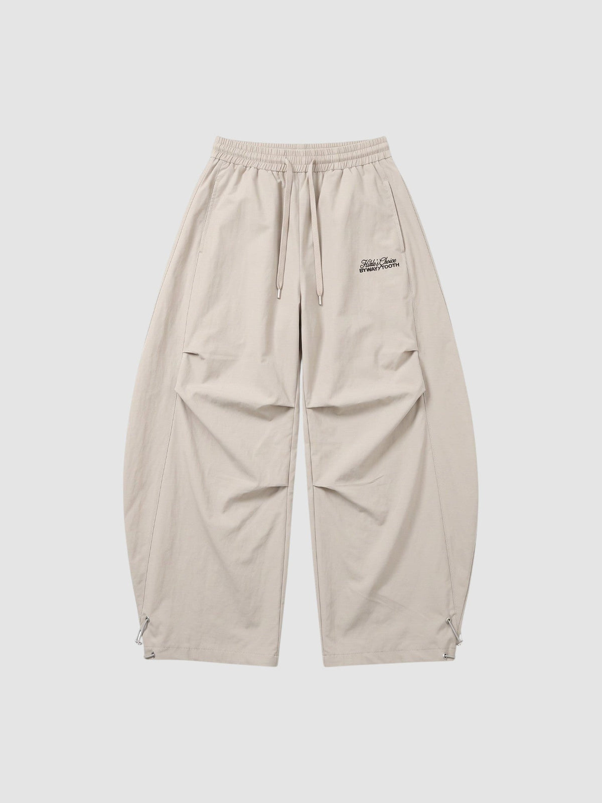 Y2K Avenue beige oversized nylon joggers with elastic waist, side pockets, and white embroidered script logo on thigh.