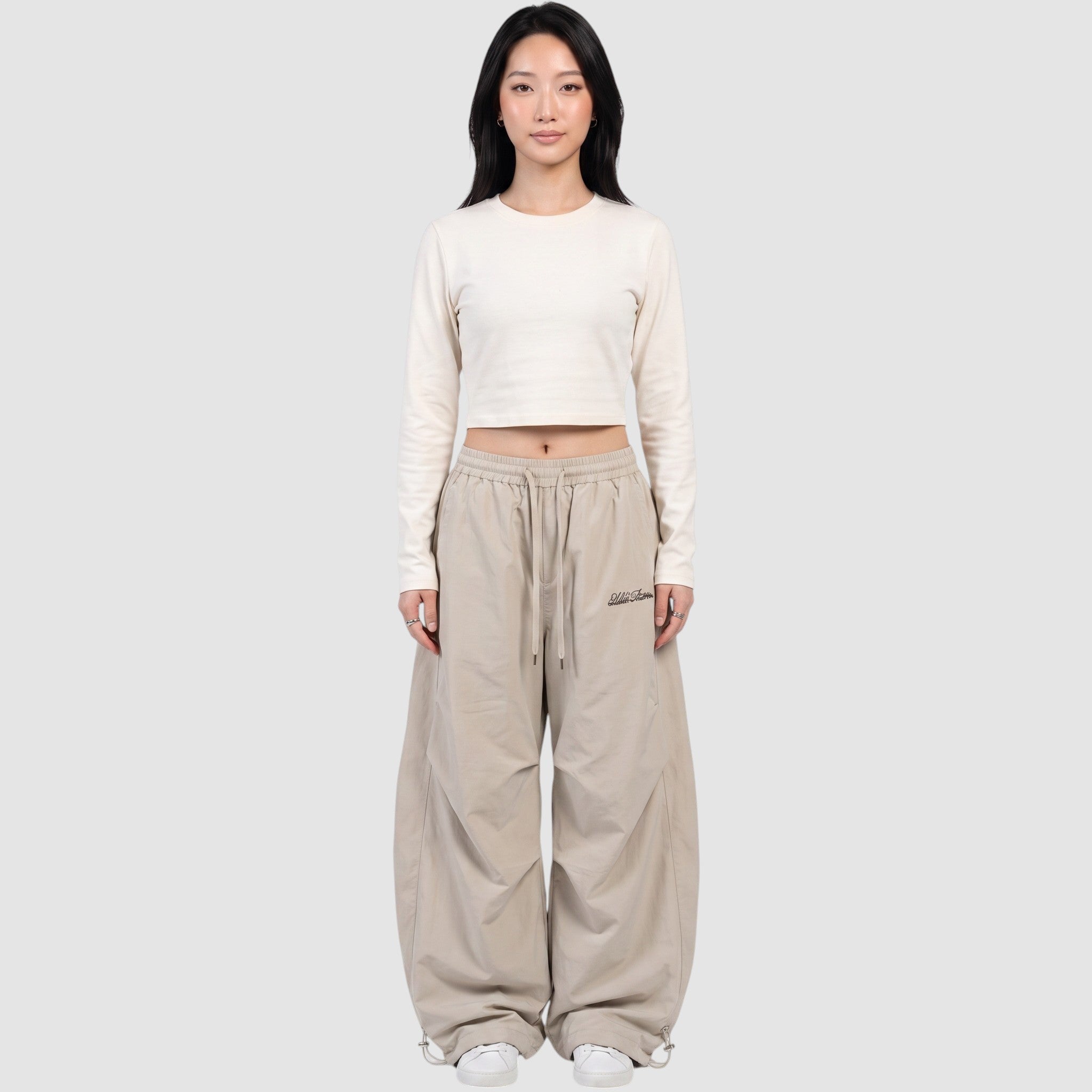 Y2K AVENUE beige oversized nylon joggers with a wide elastic waist and white embroidered logo on the right thigh.