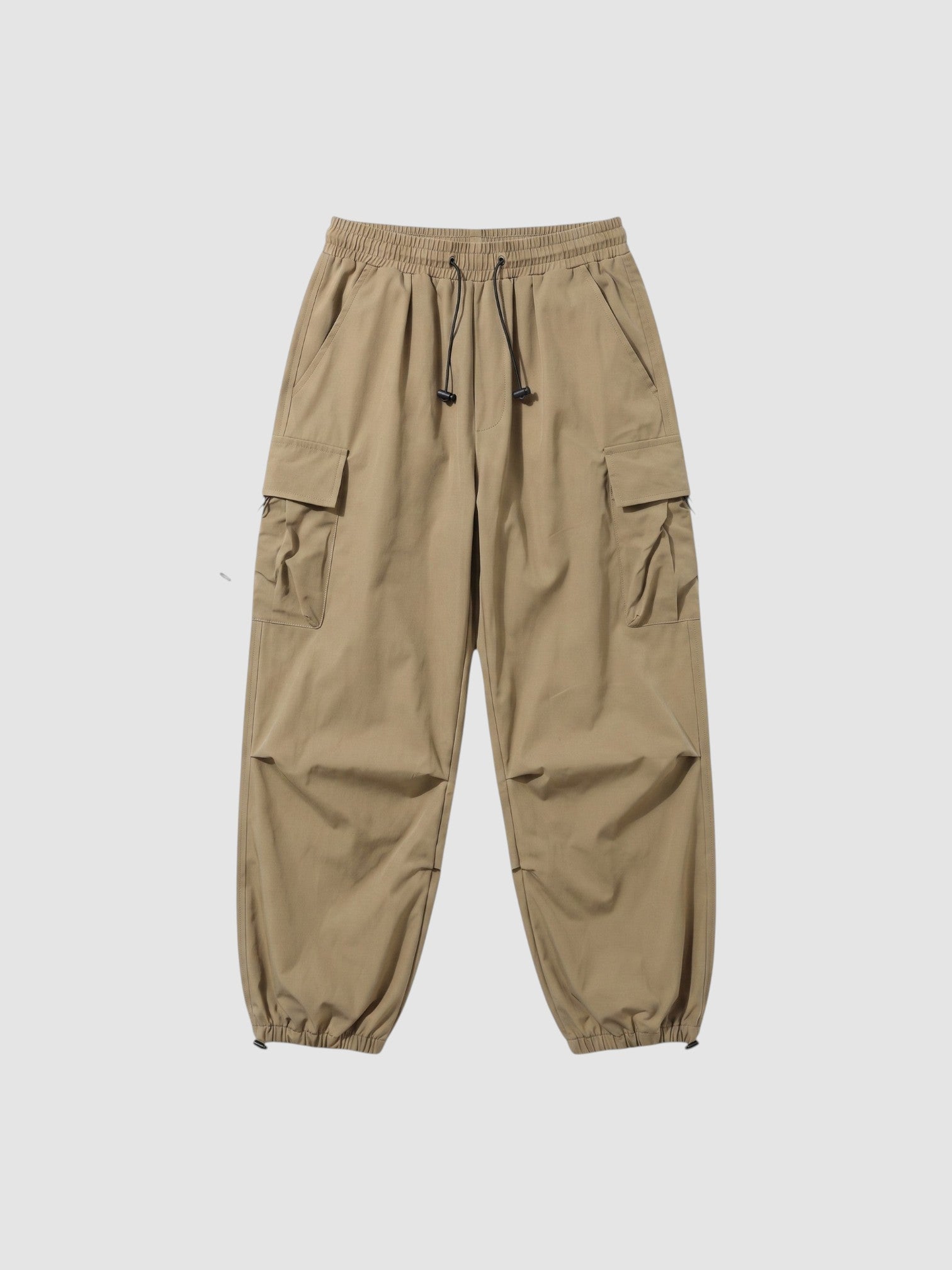Y2K Avenue beige parachute cargo pants with elastic waist, drawstring cuffs, and side flap pockets in matte fabric.
