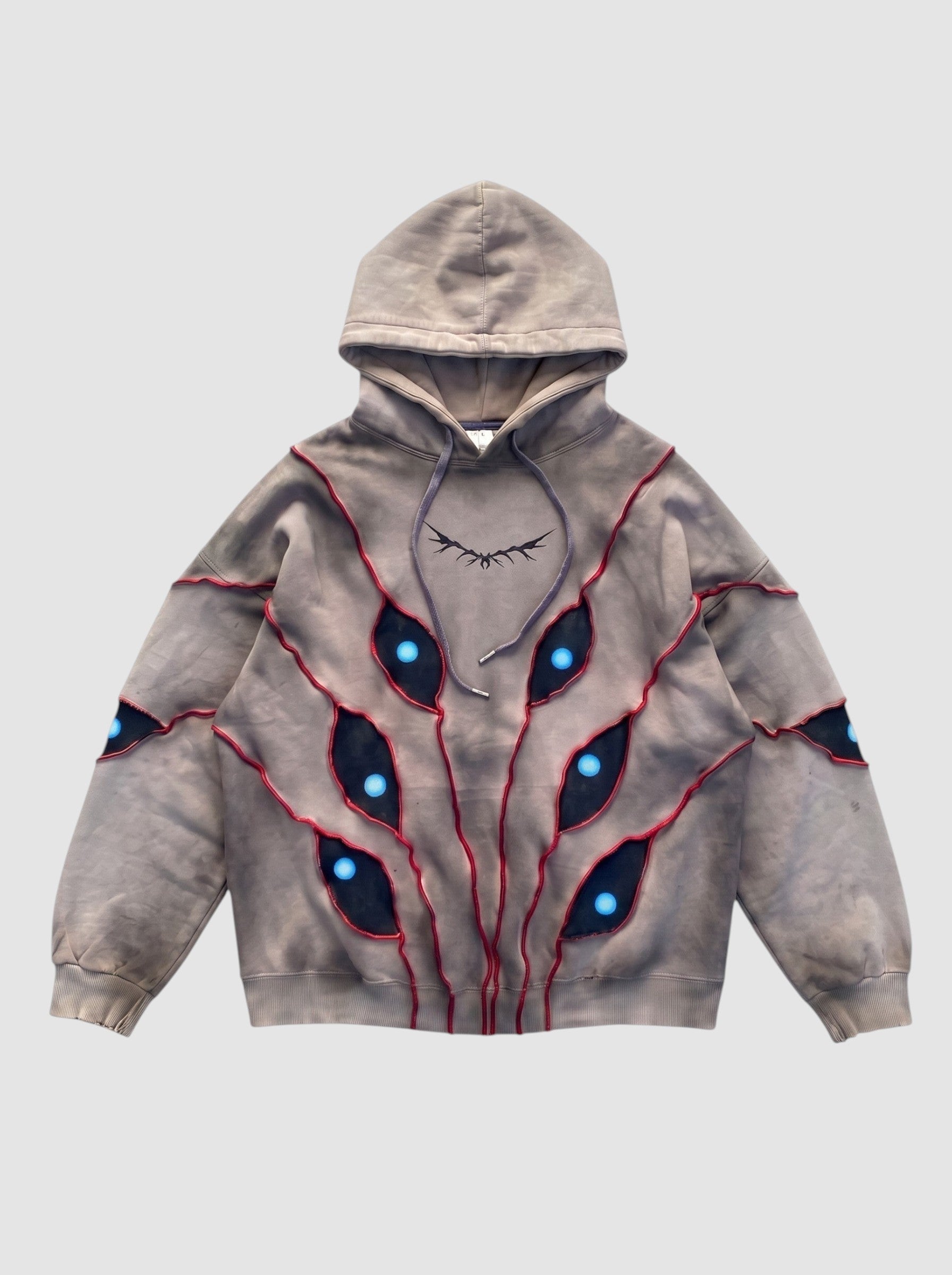 Y2K Avenue oversized beige hoodie with patchwork eye cutouts, blue pupils, and red relief stitching details.