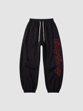 Y2K Avenue black oversize joggers with red calligraphy lettering down the leg and a cream drawstring waist.