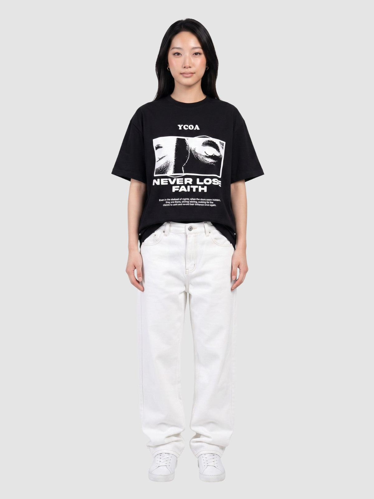 Model wearing a black Y2K Avenue oversized cotton t-shirt with a graphic print of eyes and Never Lose Faith text.