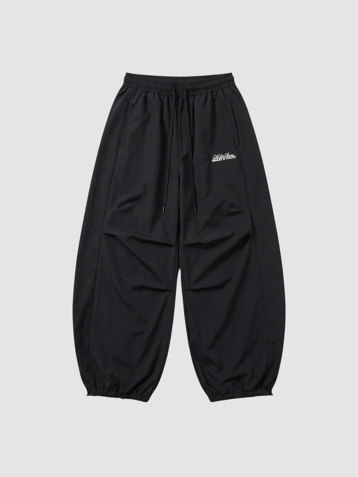 Y2K AVENUE black oversized nylon joggers with elastic waist, side pockets, and white script logo on the right thigh.