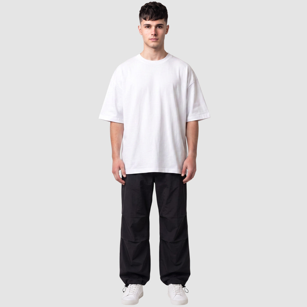 Y2K AVENUE black parachute pants with elasticated waist and adjustable ankles worn by a male model in a white tee