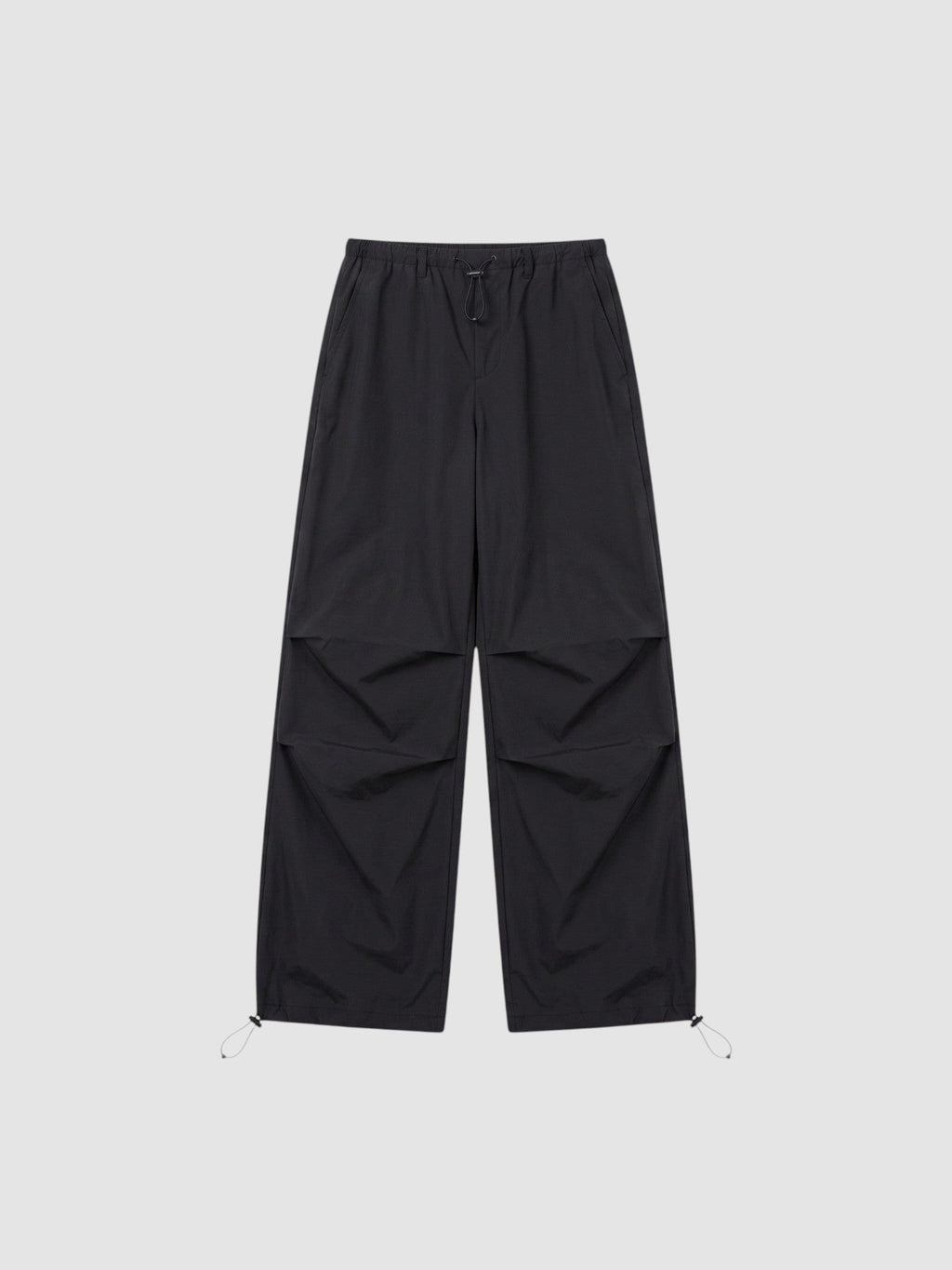 Y2K AVENUE black parachute pants with high elastic waist, adjustable drawstring cuffs, and pleated knee detailing.