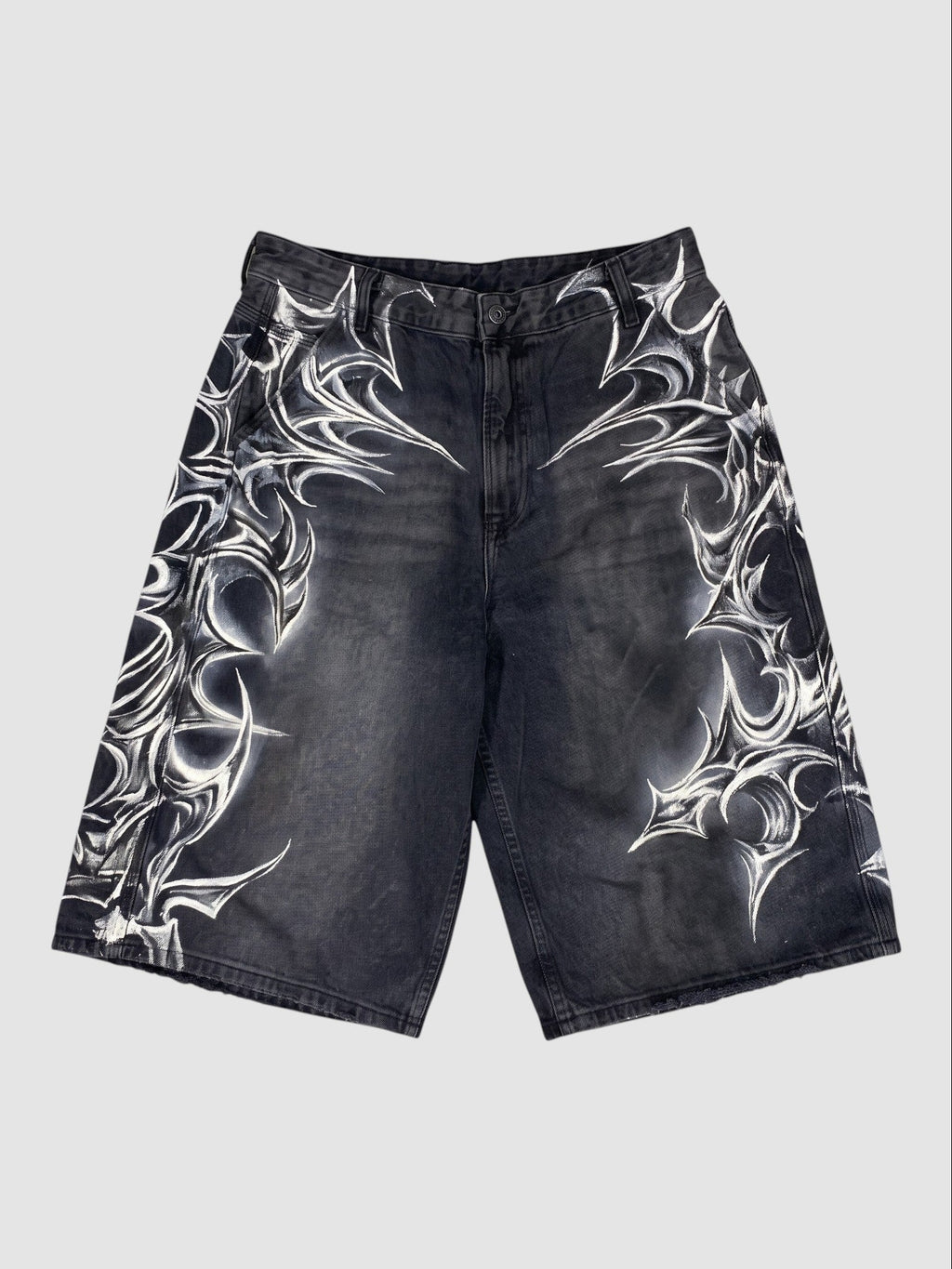 Y2K Avenue black denim jorts featuring white airbrushed tribal motifs and a loose, knee-length fit with raw hems.