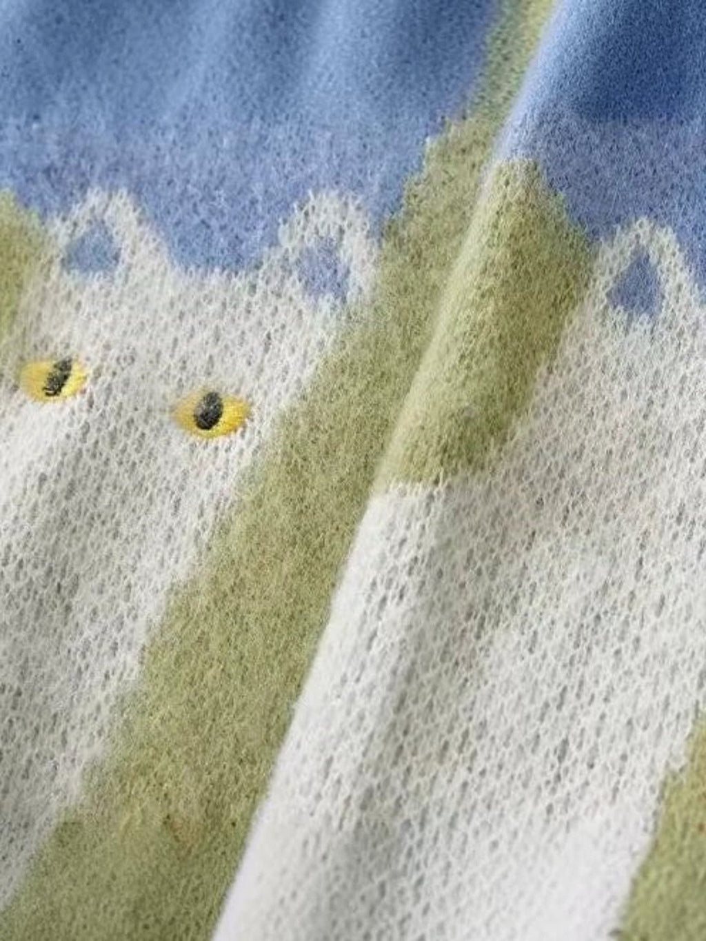 Close-up of Y2K AVENUE knit sweater featuring a cat pattern with yellow eyes on a blue and green gradient background
