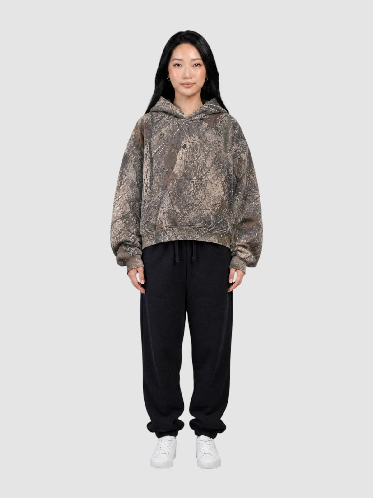 Model wearing Y2K Avenue cropped camouflage hoodie with tree bark print and boxy fit paired with black sweatpants
