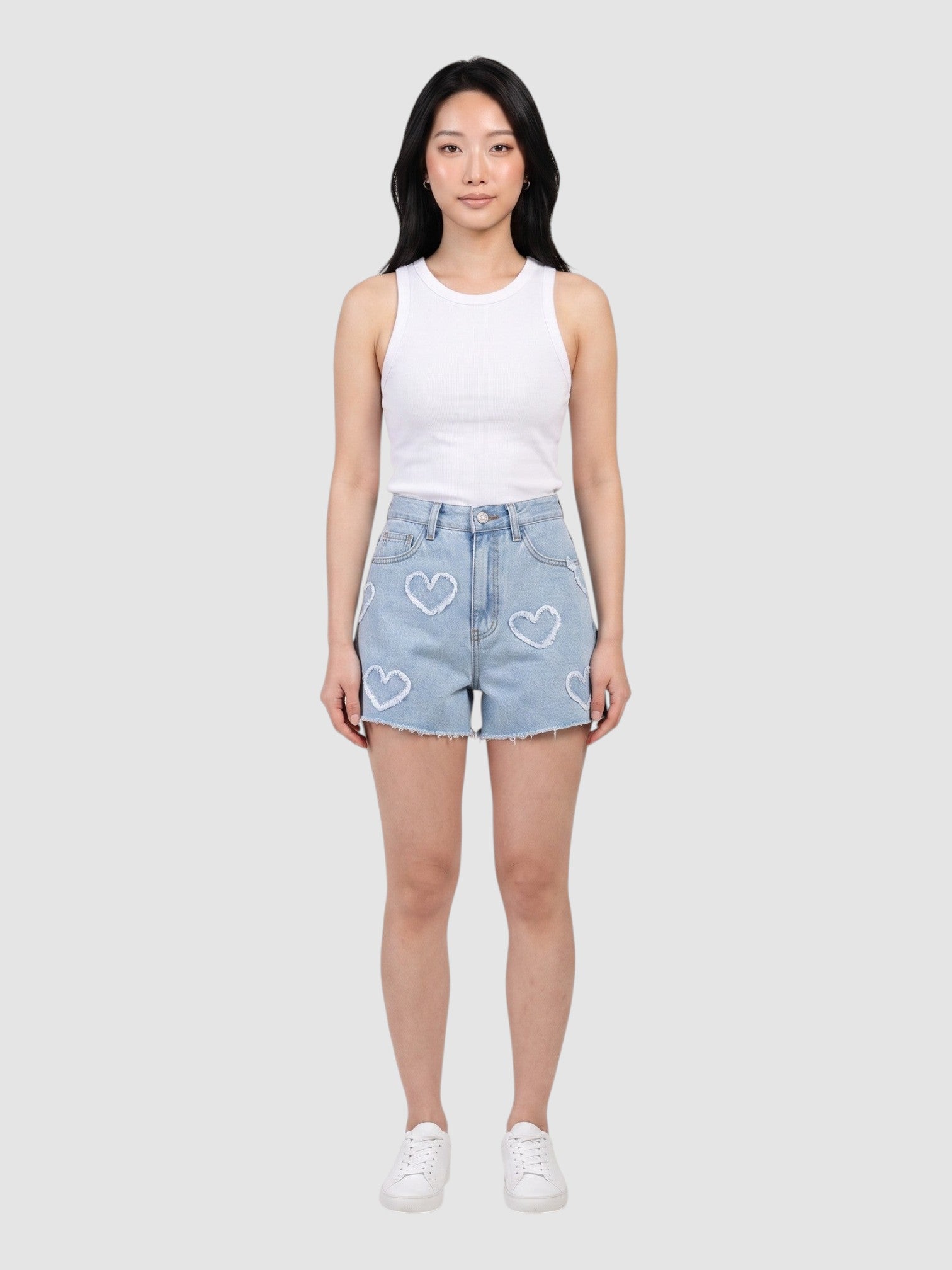 Model wearing Y2K AVENUE light blue high-waisted denim shorts with frayed heart applique details and raw hem.