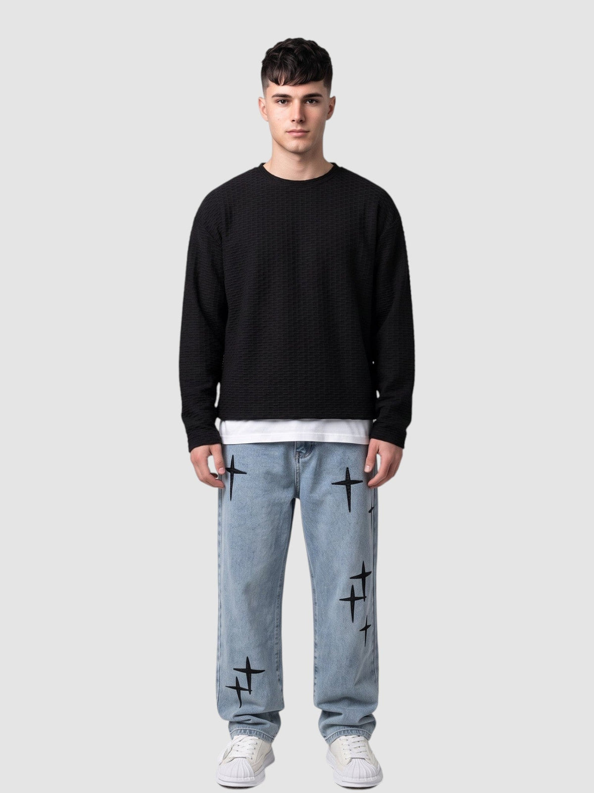 Y2K Avenue light wash denim jeans with black embroidered cross motifs worn by a man with a black textured sweater