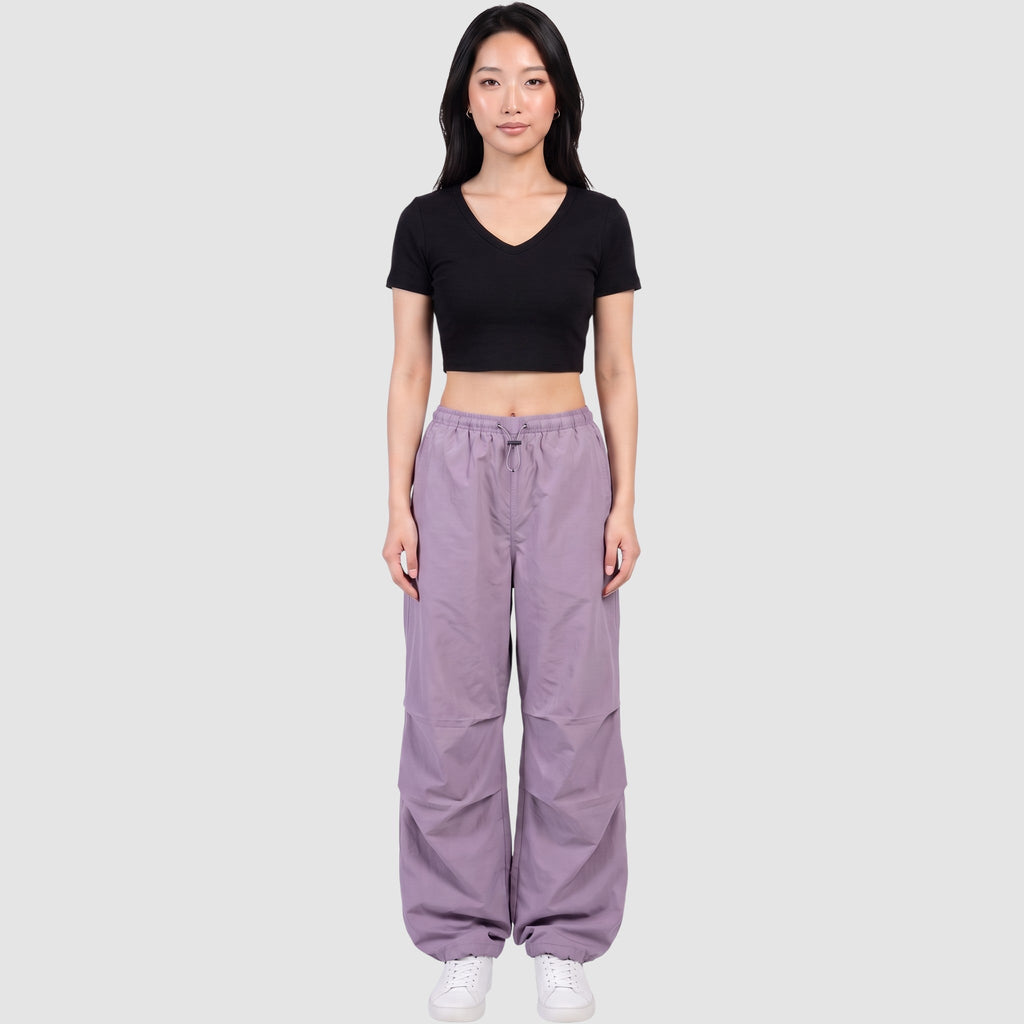 Model wearing Y2K AVENUE high-waisted purple parachute pants in matte nylon with drawstring waist and ankles.