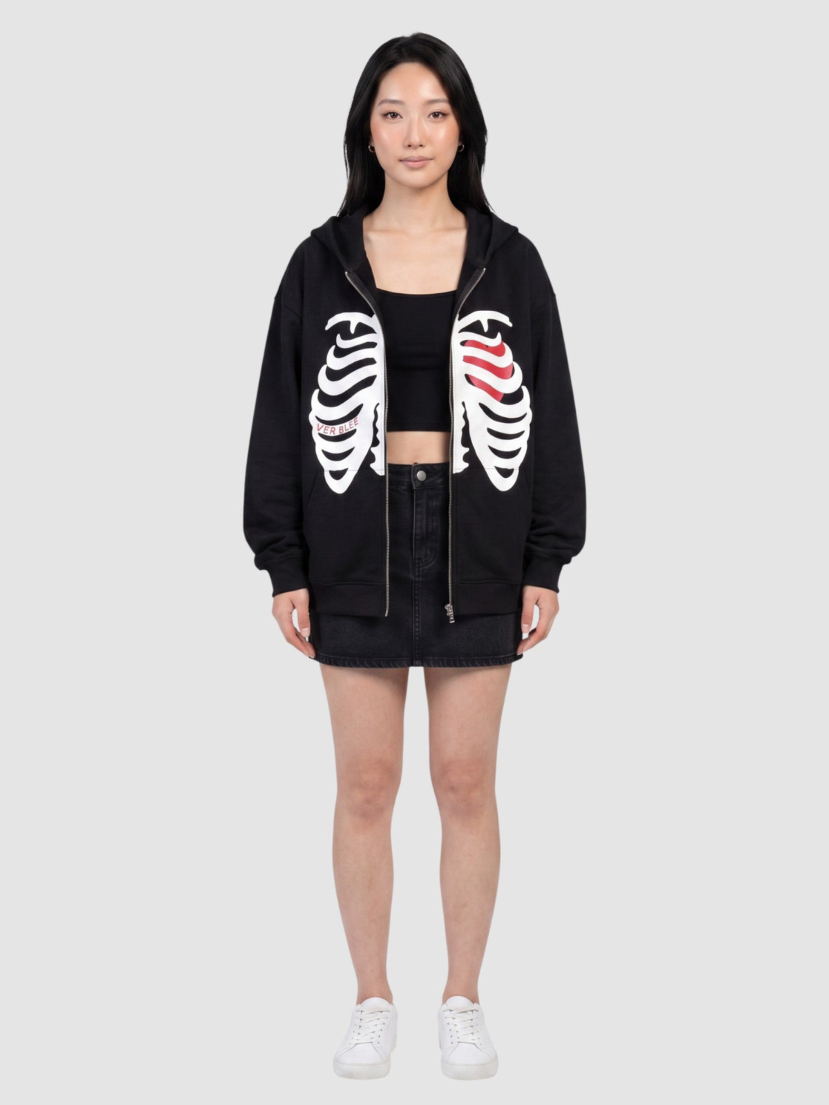 Model wearing a Y2K Avenue black zip-up hoodie featuring a white skeleton rib cage print and a red heart detail.