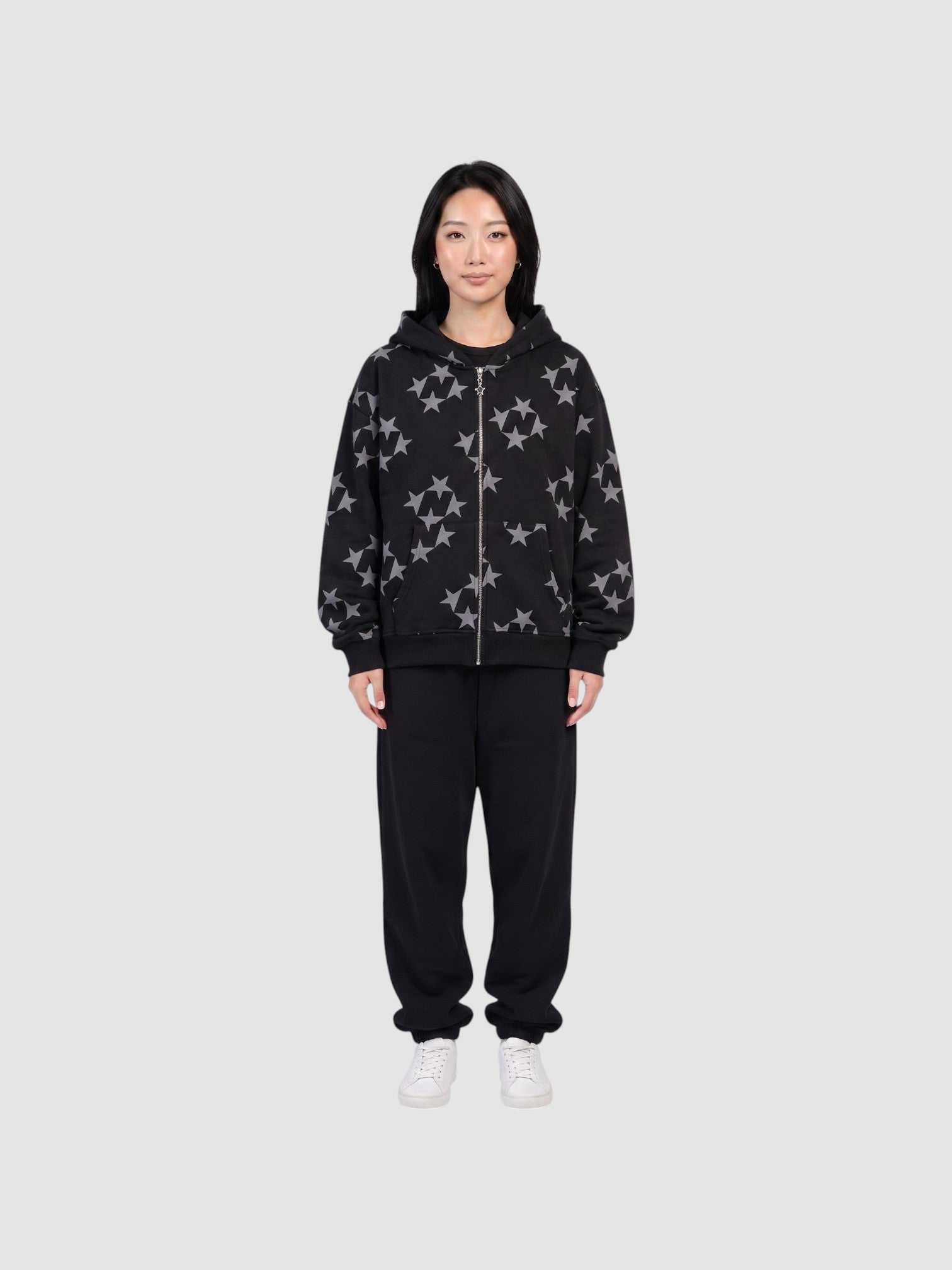 Model wearing a Y2K Avenue black zip-up hoodie with a grey all-over star print, paired with black sweatpants.
