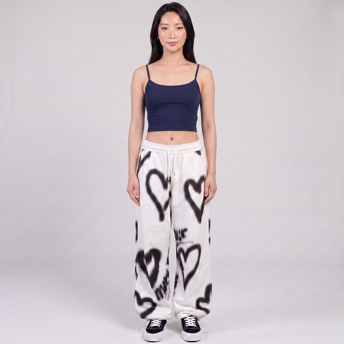 Y2K AVENUE white wide-leg sweatpants with black spray-painted heart motifs, worn with a navy crop top by a model.