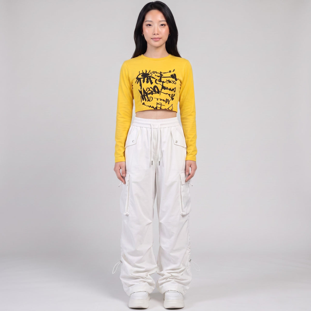 Model wearing Y2K AVENUE white high-waisted parachute cargo pants with side pockets and a yellow cropped long-sleeve top